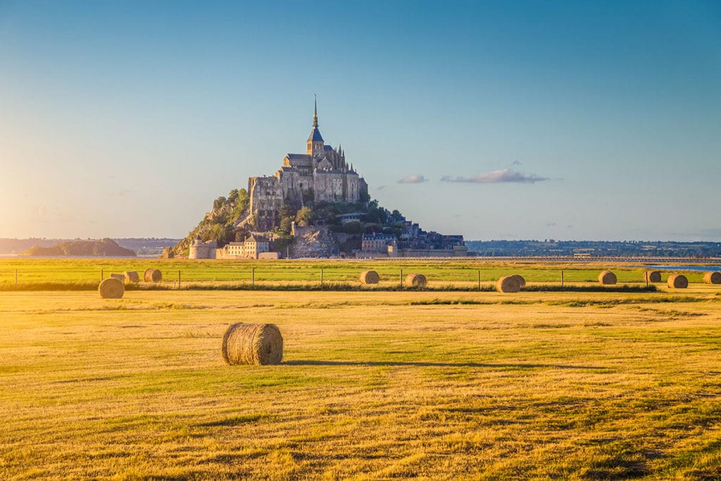 Un champ avec des rouleaux de foin et derrière le majestueux Mont Saint Michel lors d'une escapade en Normandie, des offres sur-mesure pour les familles, groupes d'amis, scolaires, entreprises et associations